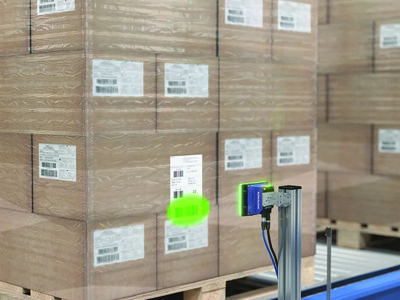 Escáner industrial verificando la etiqueta logística de un palet de cajas antes de su carga en el camión